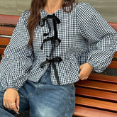 Person wearing a black and white checkered blouse with black ribbons sitting on a wooden bench.